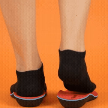 Black-socked feet demonstrating red and black orthotic inserts on an orange background.